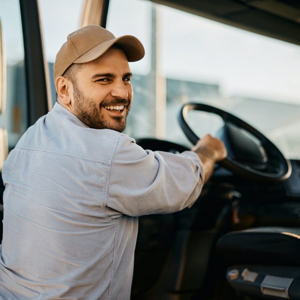 Ein LKW Fahrer, der in seinen LKW einsteigt und dabei lächelnd in die Kamera schaut